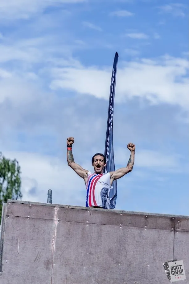 Løper med armene i været på toppen av muren under Bootcamp Survivor